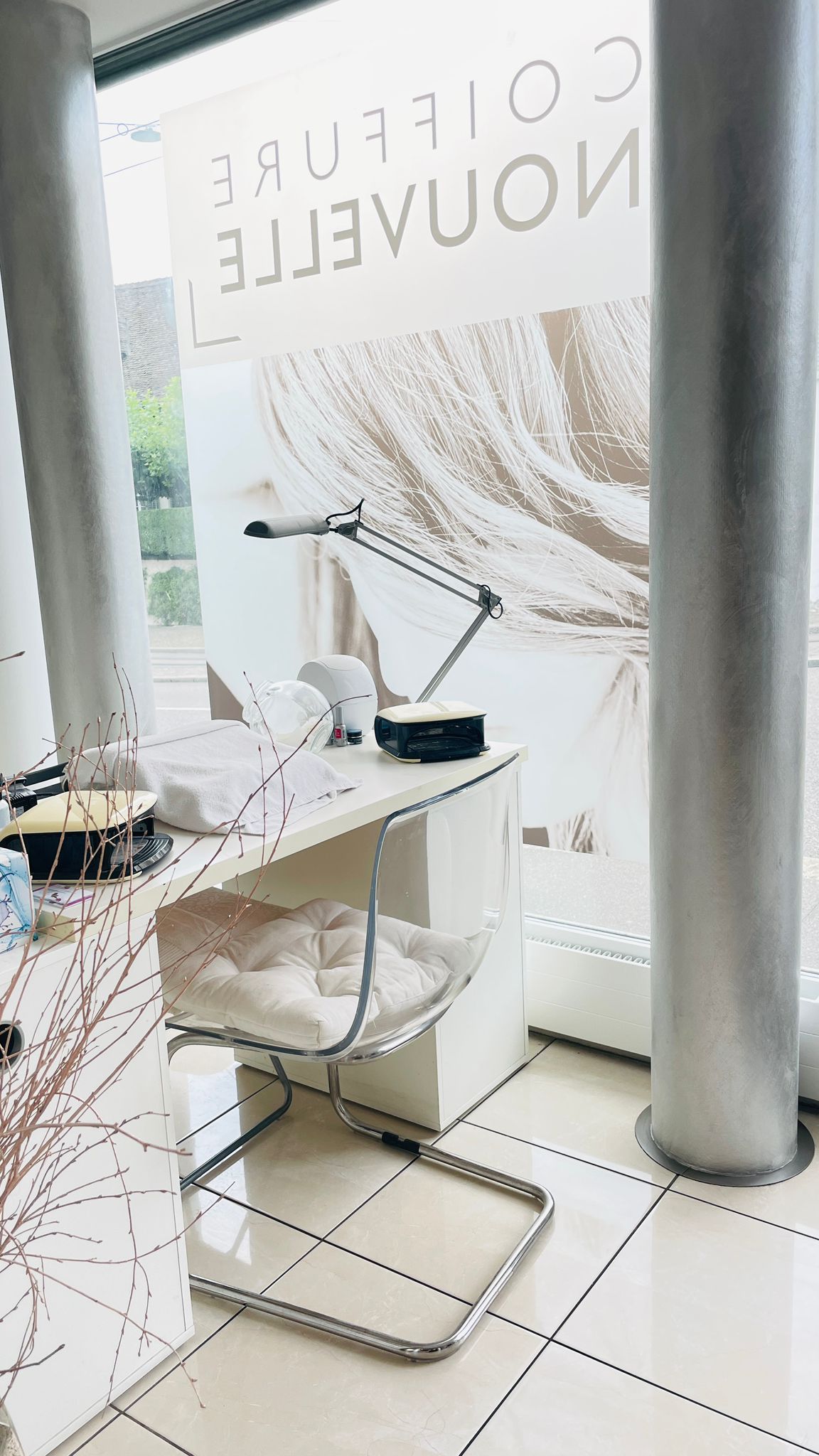 Saloneinrichtung mit Schreibtisch, Stuhl und Werbung am Fenster; Farbgebung in Weiß und Silber.