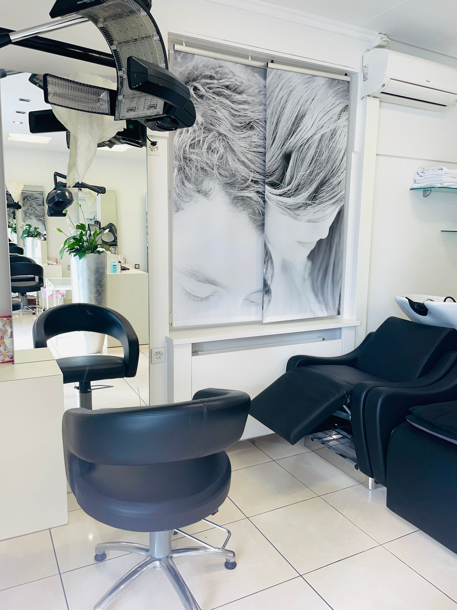 Inneneinrichtung eines Friseursalons: schwarzer Stuhl, Haartrockner, verstellbarer Waschsessel, Kunstwerk eines Gesichts.