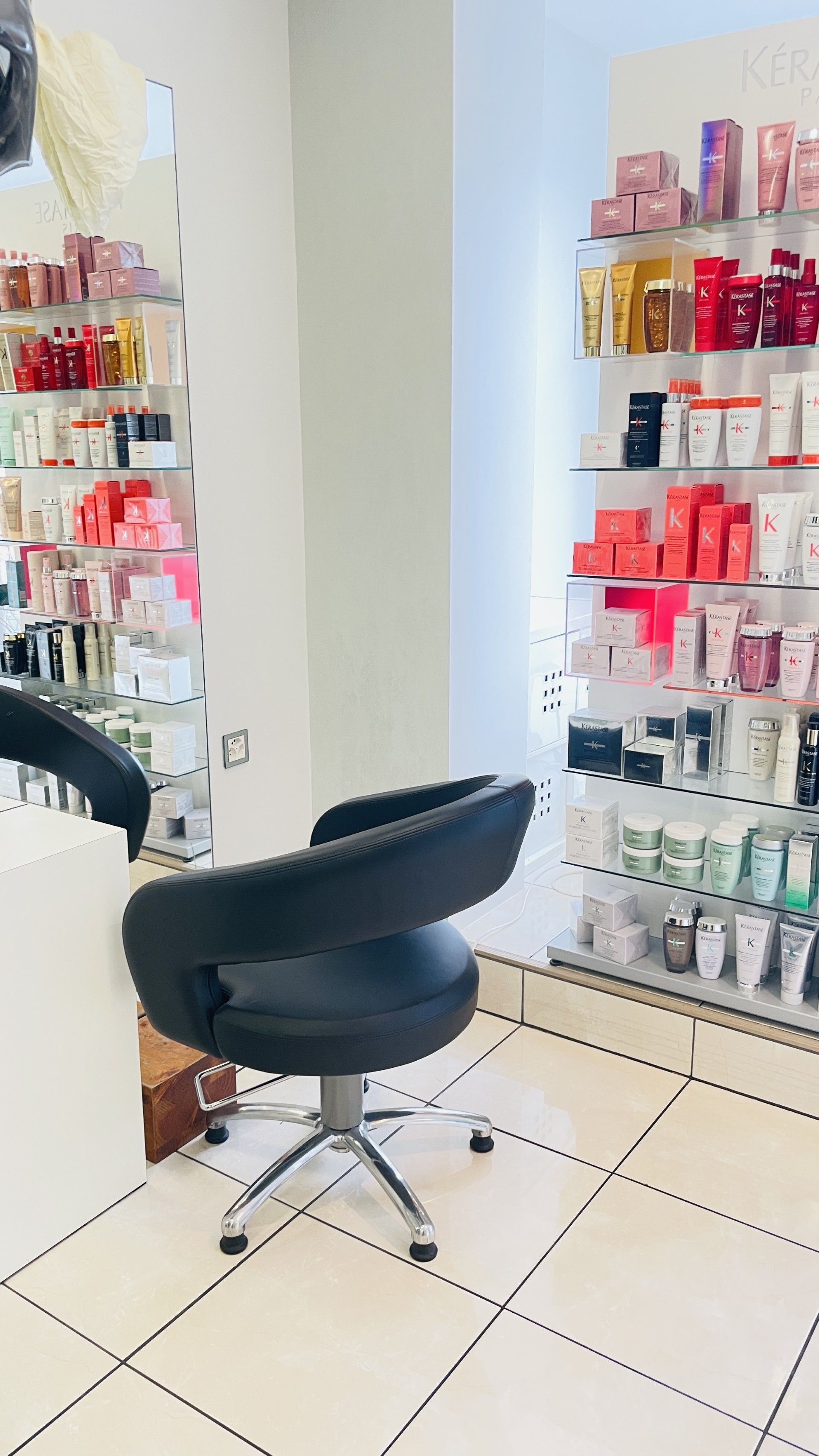 Friseursalon-Interieur mit schwarzem Stuhl, Produkten auf Regalen und heller Beleuchtung.