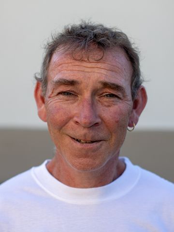 Mann mit heller Haut, bekleidet mit einem weissen Hemd, lächelt leicht. Aussenaufnahme, neutraler Hintergrund.