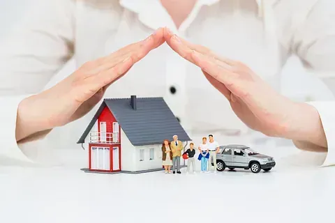 Una mujer cubre una casa y un coche con sus manos.