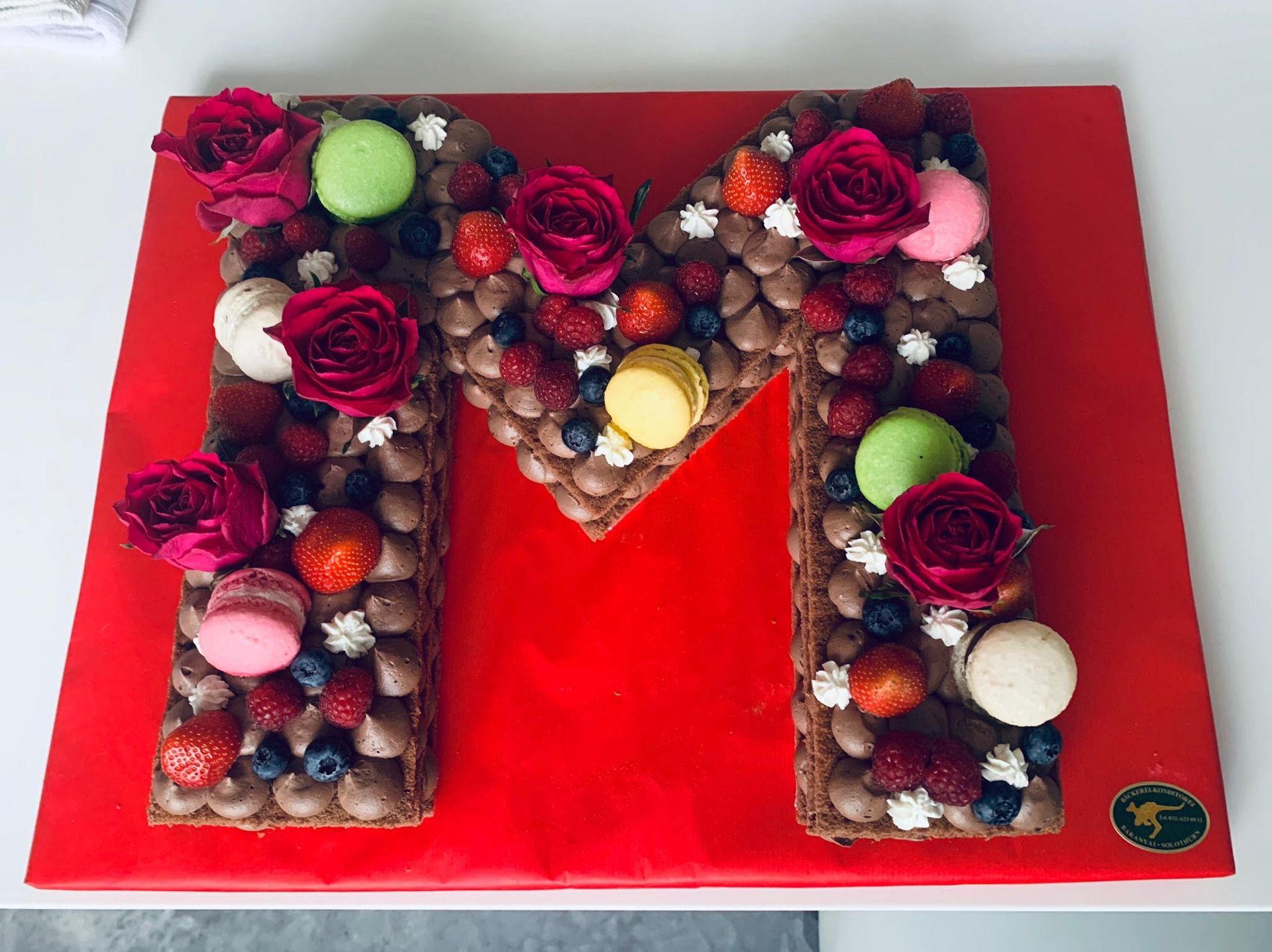 Auf einem roten Teller liegt ein Kuchen in Form des Buchstabens M.