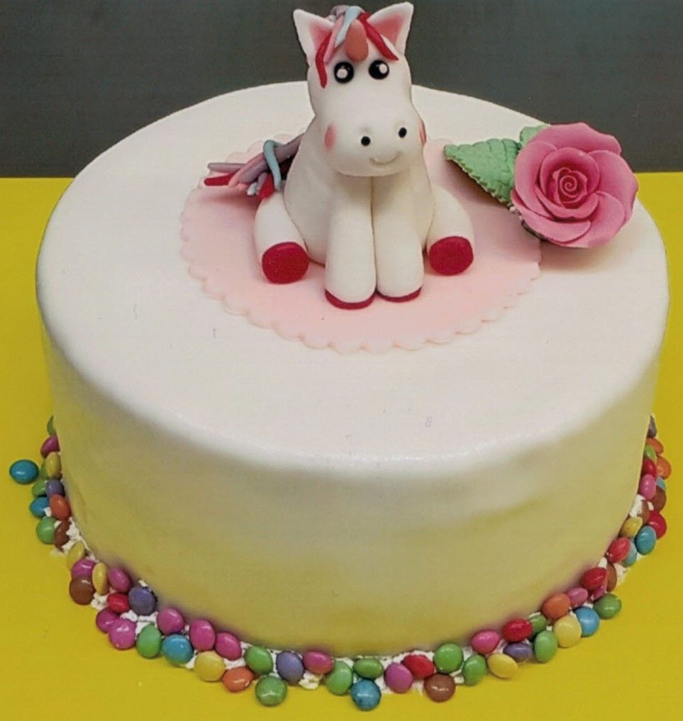 Ein weißer Kuchen mit einem Einhorn und einer rosa Rose oben drauf