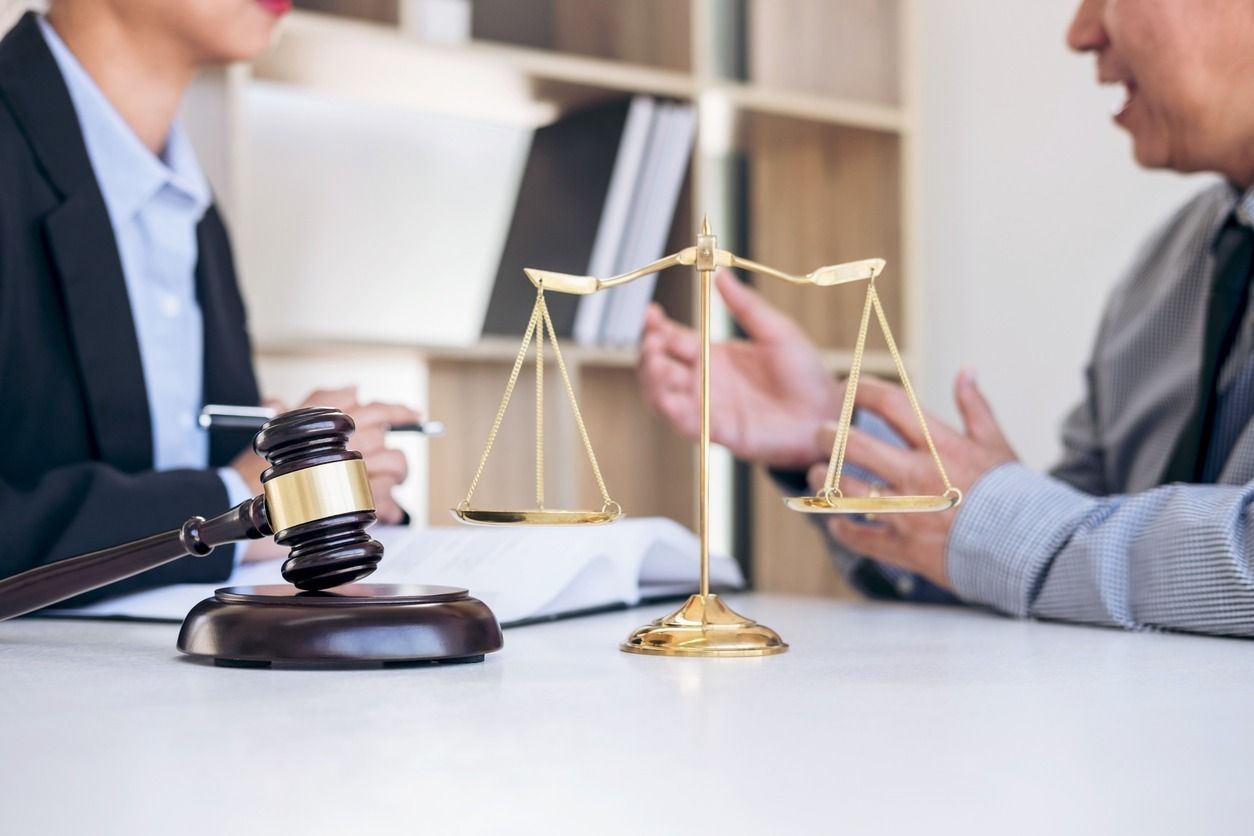 Un abogado y un cliente discuten un caso en un escritorio con un mazo y una balanza de la justicia.