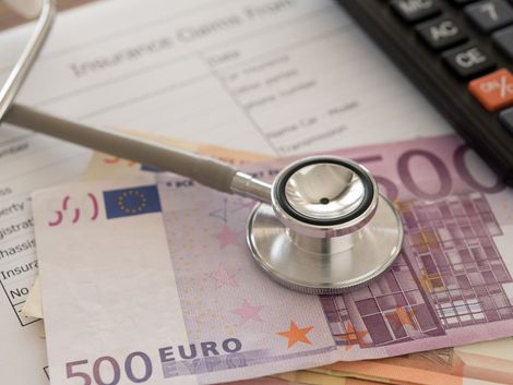 Un estetoscopio reposa sobre una pila de billetes de euro, una calculadora y un formulario de reclamación de seguro.