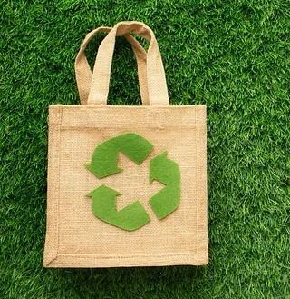 Una pequeña bolsa con un símbolo de reciclaje verde se encuentra sobre un exuberante campo verde.