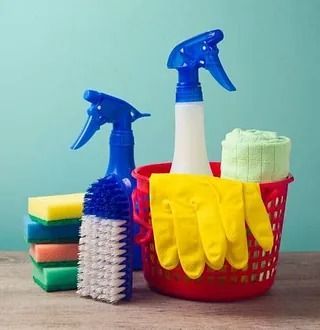 Una canasta llena de productos de limpieza, incluidas botellas de spray, esponjas, cepillos y guantes.