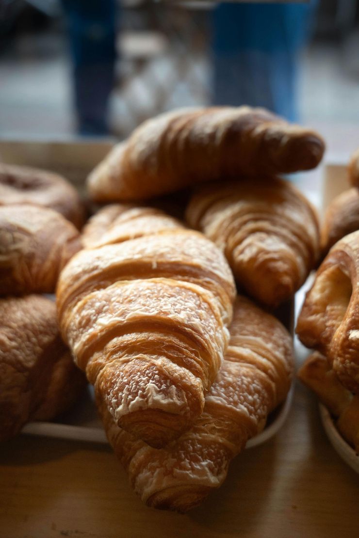 Bandeja de croissants dorados en el mostrador de una panadería, con capas hojaldradas y un fondo desenfocado.