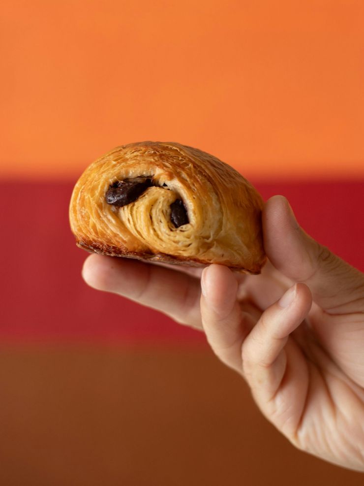 Mano sosteniendo un hojaldre de chocolate sobre un fondo naranja.