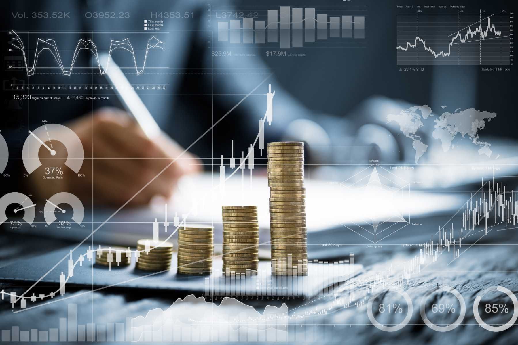 Monedas apiladas en fila con gráficos financieros superpuestos y una persona escribiendo en el fondo.