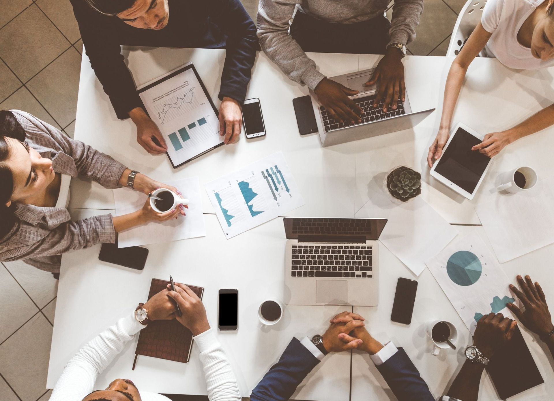 Reunión de equipo de negocios alrededor de una mesa blanca, revisando datos en gráficos y computadoras portátiles.