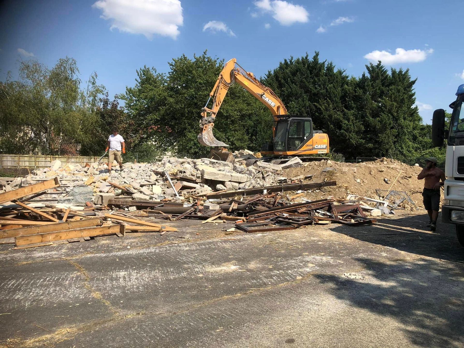 Une pelleteuse jaune démolit un bâtiment, laissant derrière elle un tas de gravats et de débris.