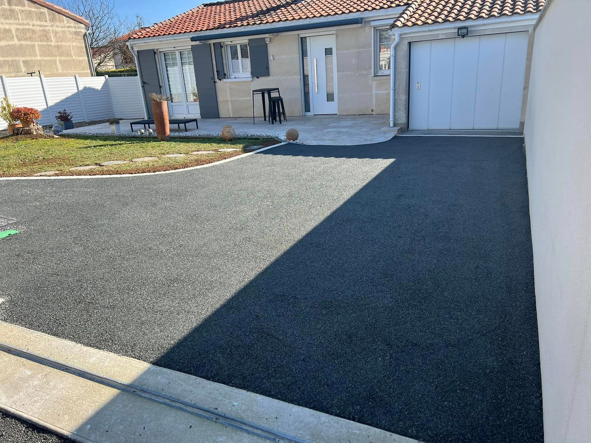 Une allée de gravier mène à une petite maison de plain-pied avec une porte de garage blanche et un salon de jardin.