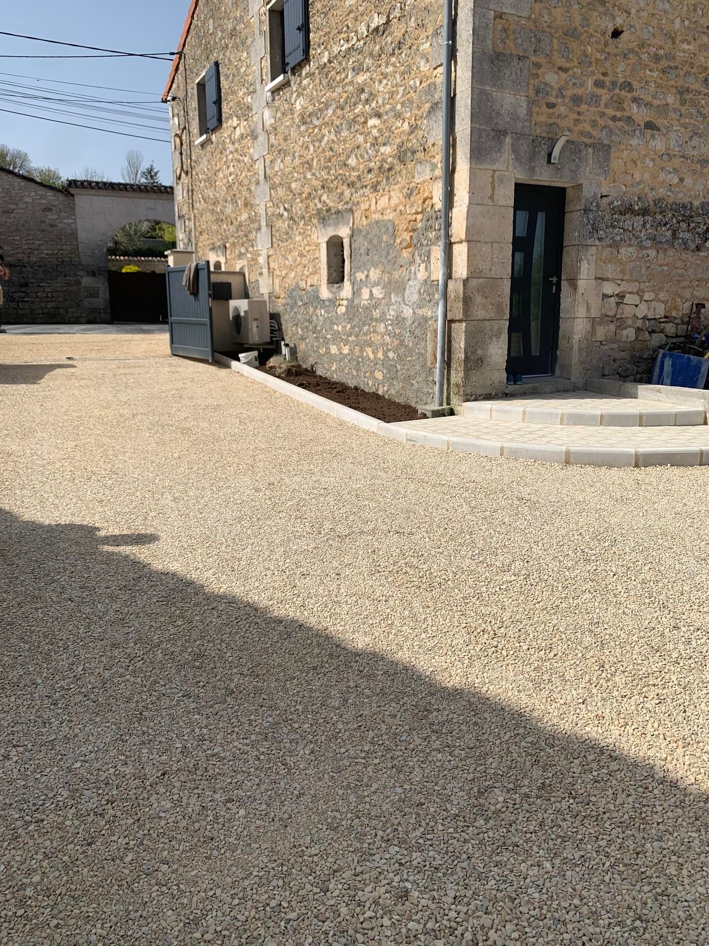Une maison en pierre avec une cour gravillonnée, un petit parterre de jardin le long du mur.