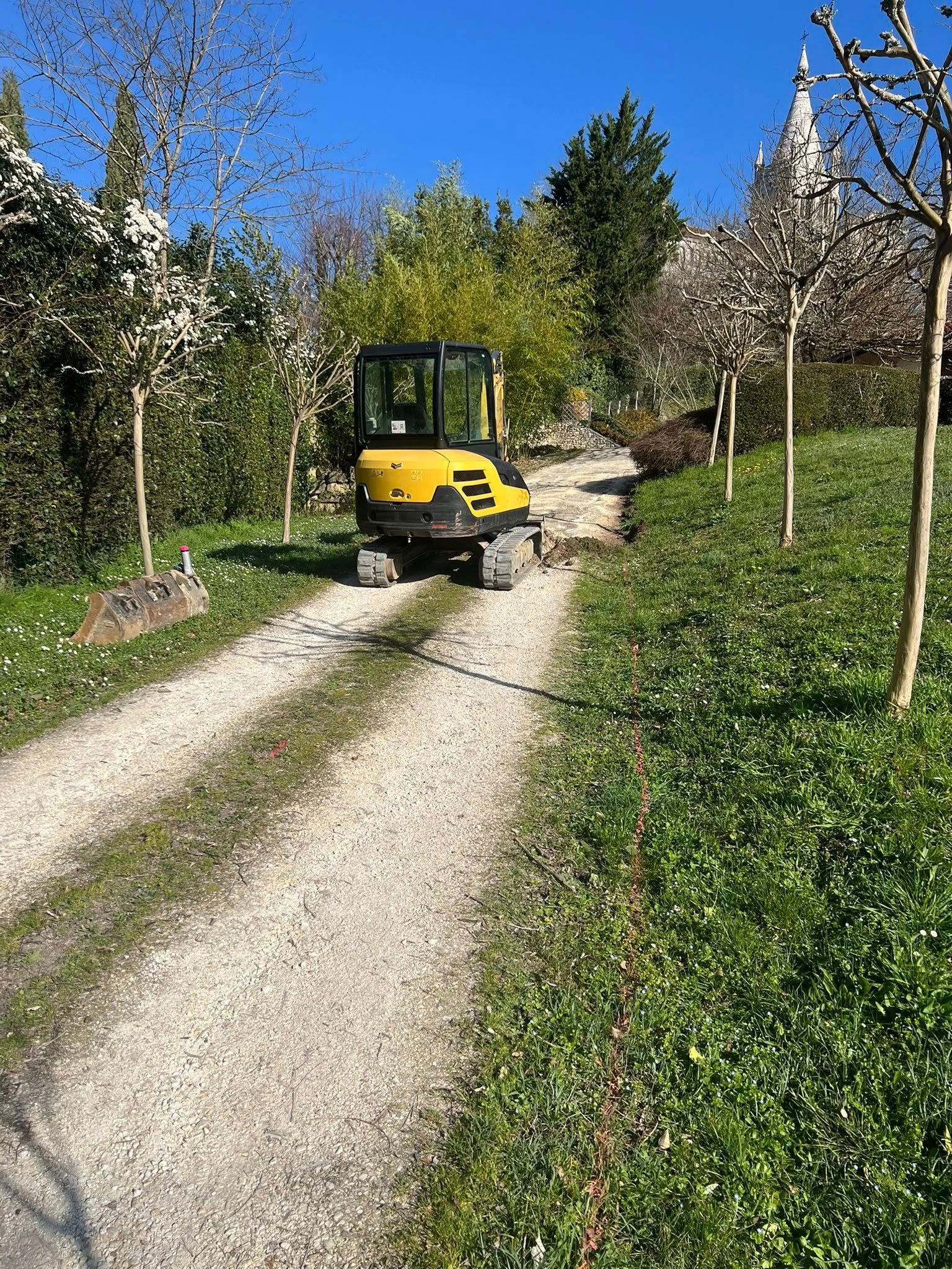 Une petite pelleteuse jaune garée sur un chemin de gravier bordé d'arbres.