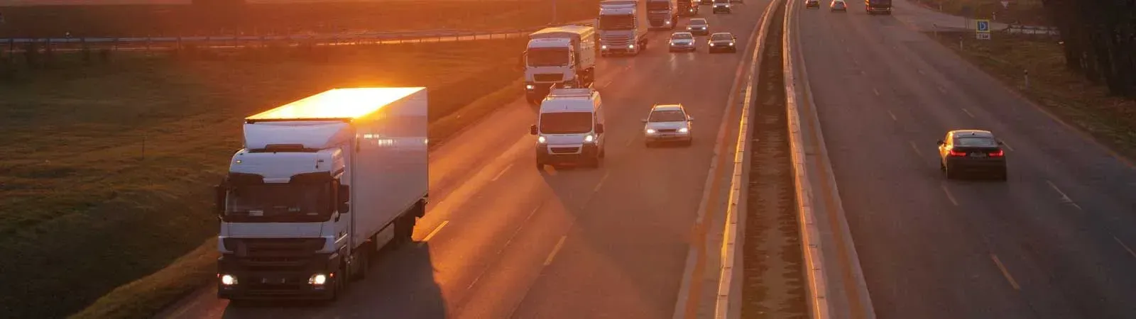 Una fila de camiones circula por una autopista al atardecer.