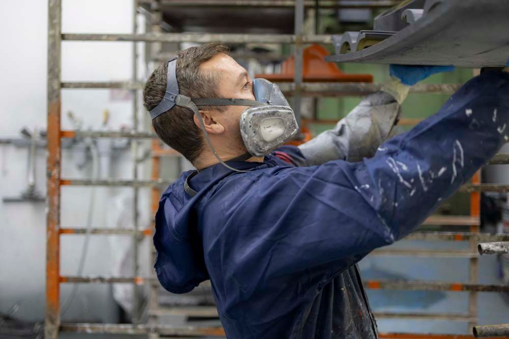 Ein Mann mit Gasmaske und Schutzbrille arbeitet an einem Auto.