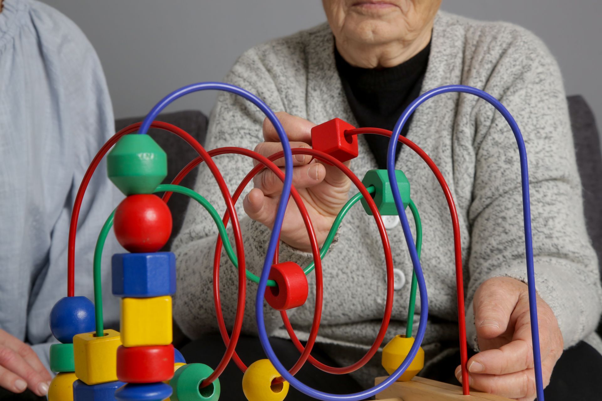 Des adultes âgés utilisent un jouet coloré en fil de fer et perles sur une table, leurs mains faisant passer les pièces à travers des boucles.