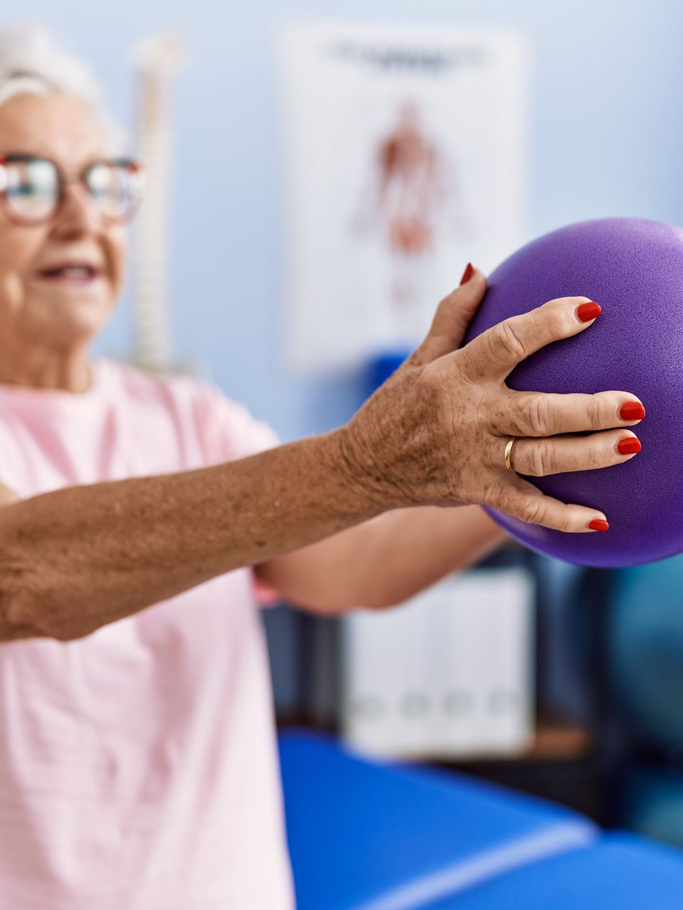 Une personne âgée tenant un ballon d'exercice violet dans une salle.