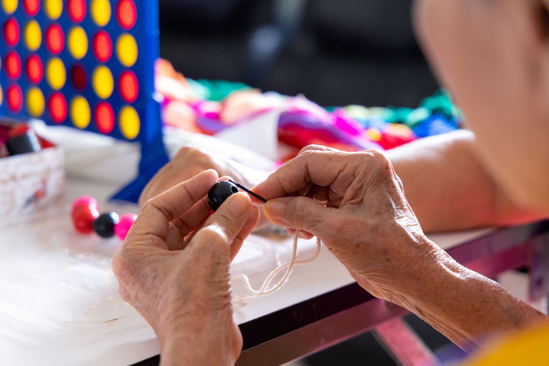 Des mains enfilent un fil transparent, avec un jeu de Puissance 4 coloré en arrière-plan.