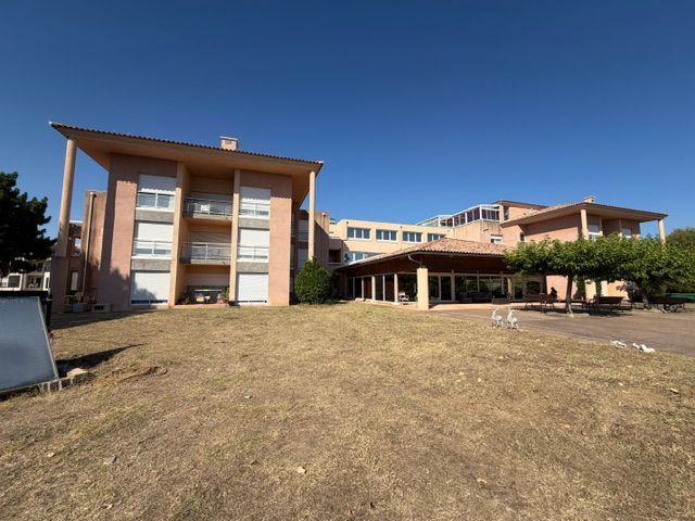 Immeuble moderne à plusieurs étages d'un EHPAD, aux murs beiges et aux grandes fenêtres, sous un ciel d'un bleu limpide.