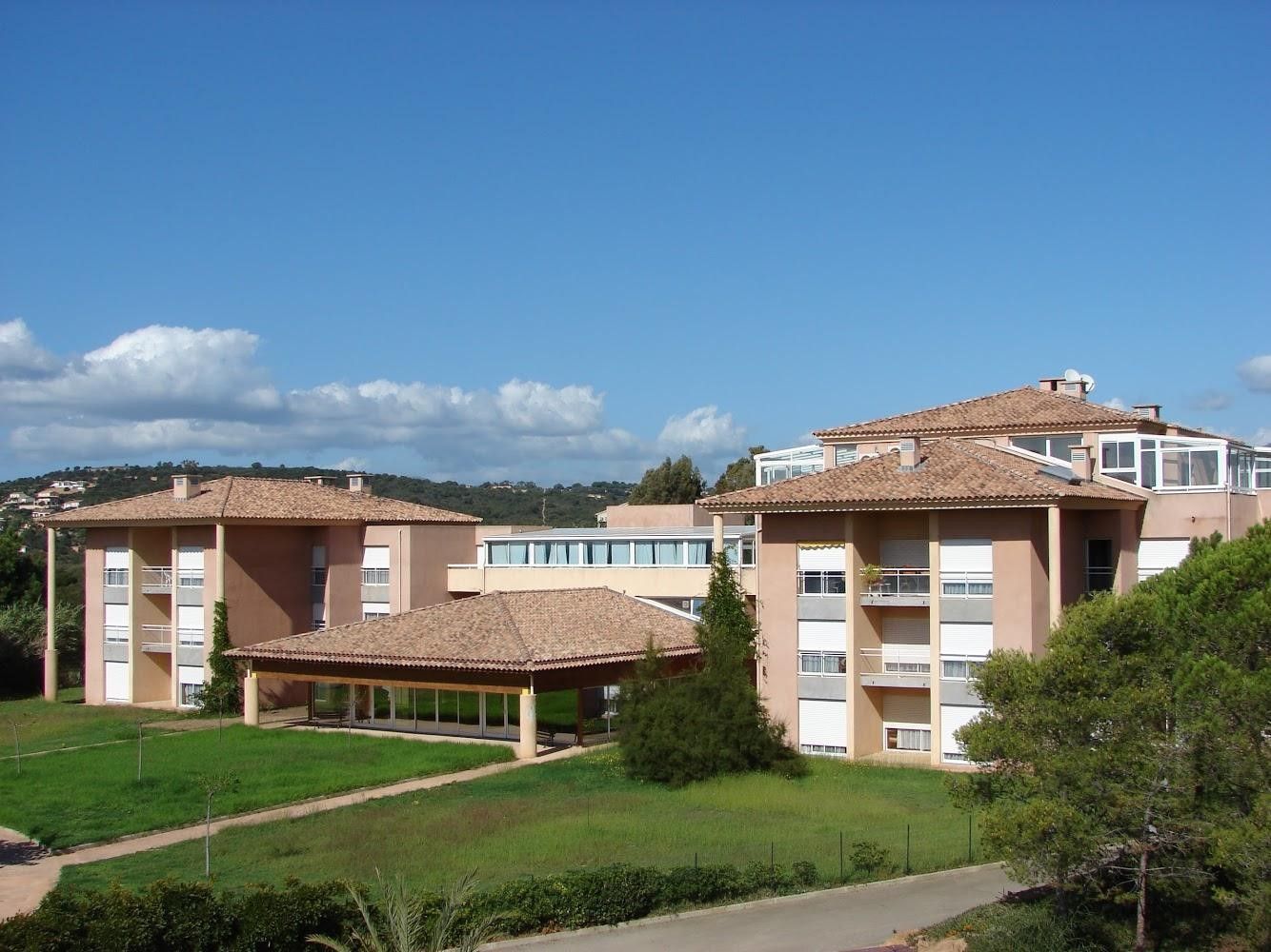 Résidence séniors aux toits de tuiles et balcons bordant une pelouse verdoyante sous un ciel bleu.