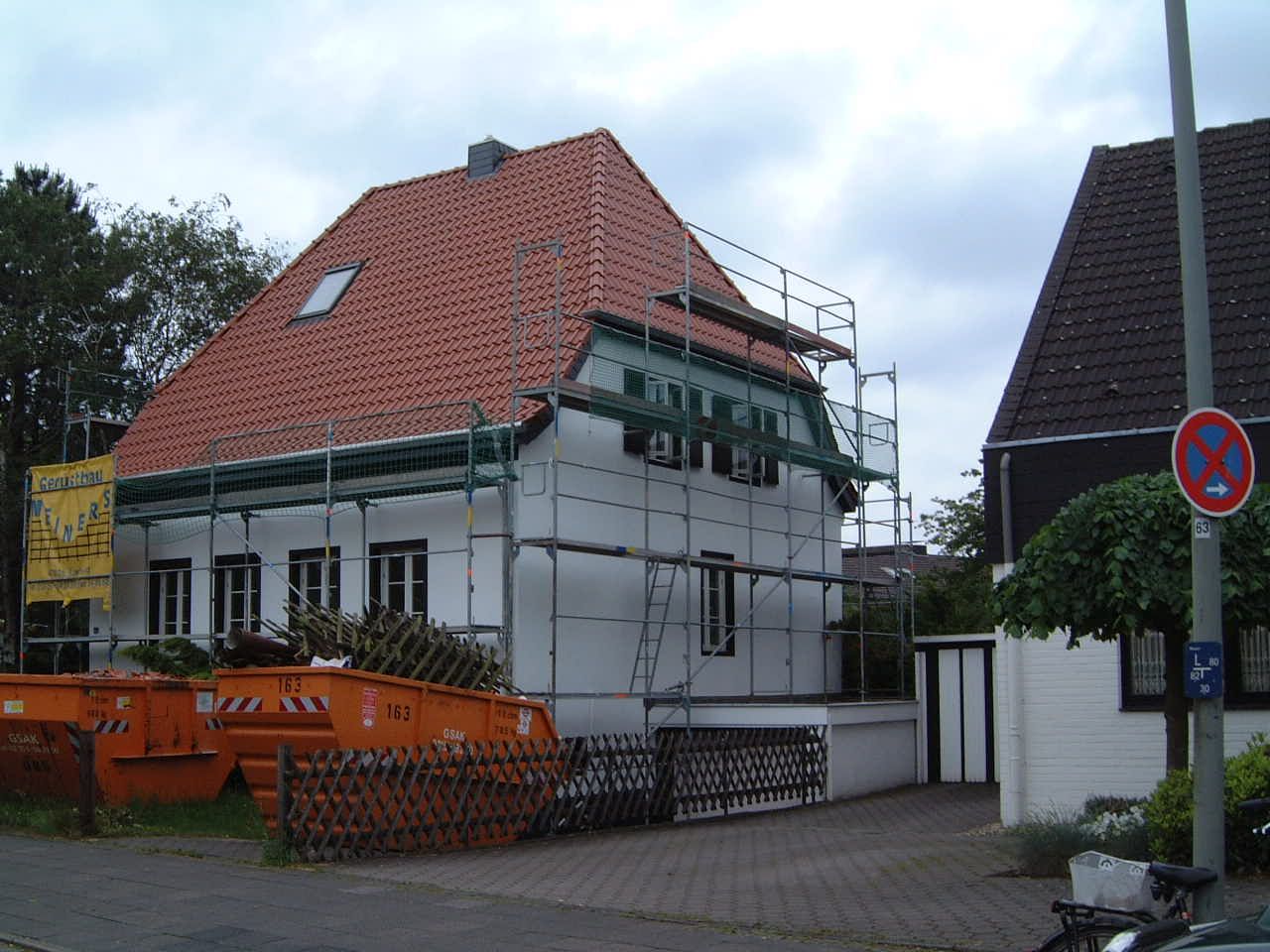 ein weißes Haus mit Baugerüst und rotem Dach