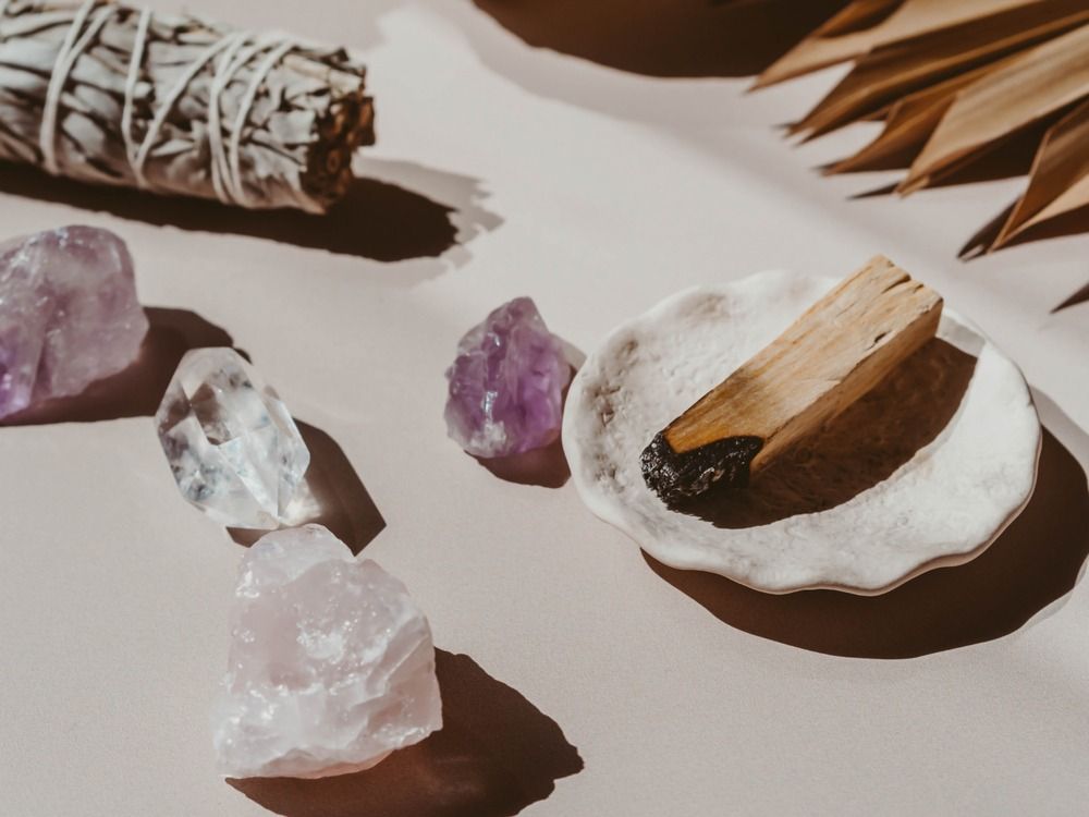 Cristales de amatista, manojo de salvia, palo de Palo Santo y un plato, dispuestos sobre una superficie neutra con sombras.