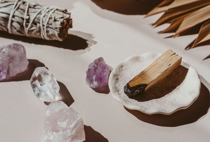 Cristales de amatista, manojo de salvia, palo de palo santo y un cuenco de conchas marinas sobre una superficie blanca.