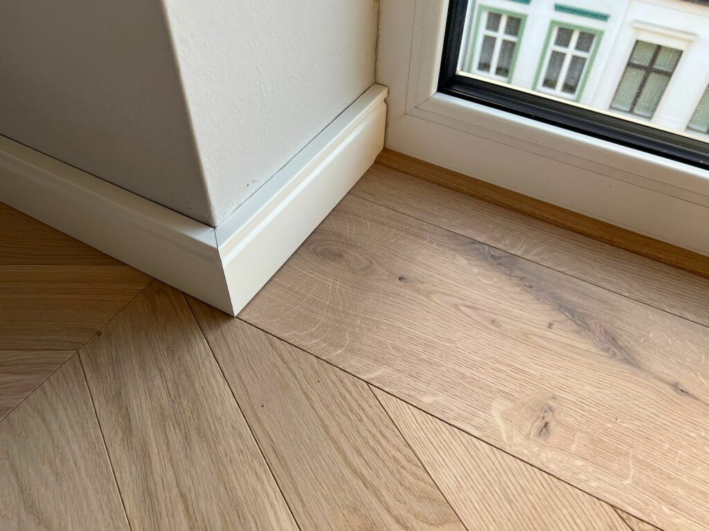 Eine Nahaufnahme eines Holzbodens neben einem Fenster.