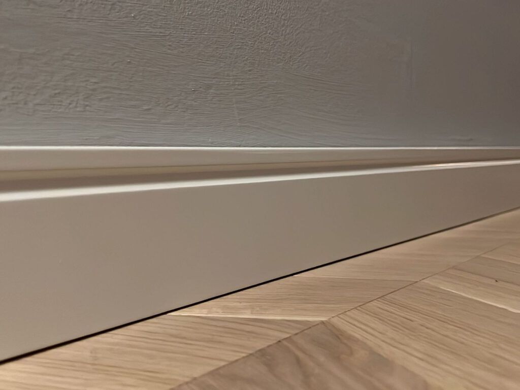 Eine Nahaufnahme einer weißen Fußleiste auf einem Holzboden.