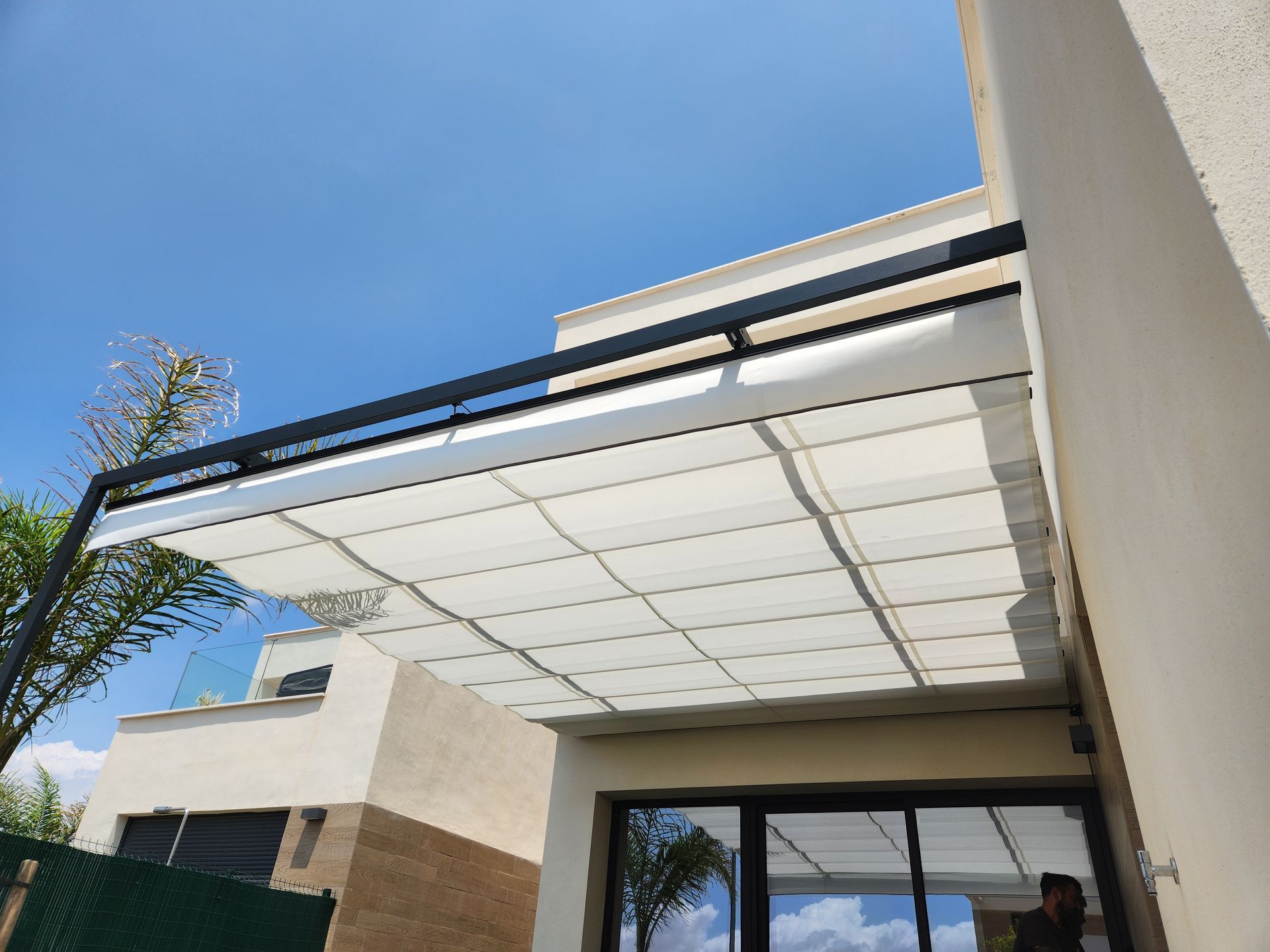 Pérgola blanca sobre patio, sostenida por un marco negro, contra el cielo azul.