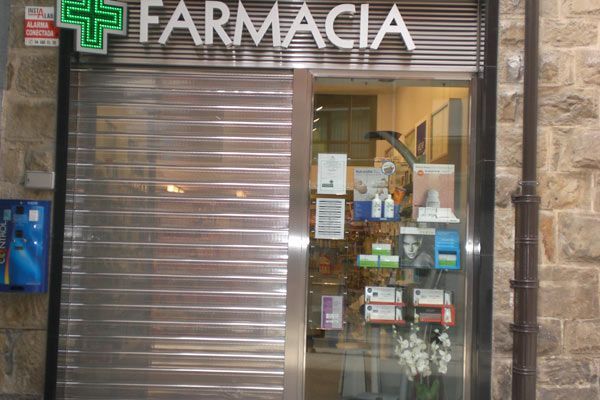 El frente de una farmacia con una cruz verde en el cartel.