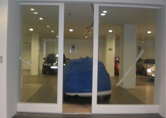 Un coche azul está detrás de una puerta de cristal en una sala de exposición.