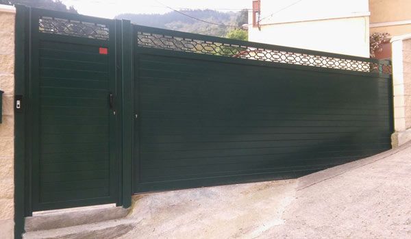 Una puerta negra está en la cima de una colina, al lado de una pared de ladrillos.