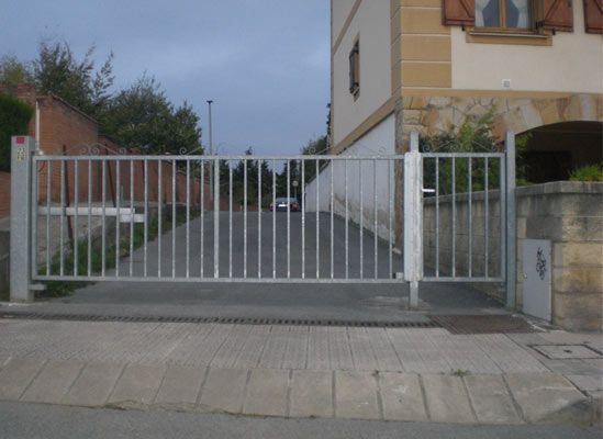 Una puerta de metal está abierta a un camino de entrada frente a una casa.