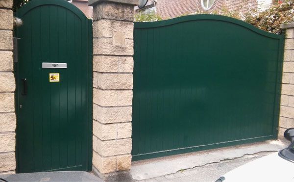 Una puerta verde y un coche blanco están aparcados delante de una pared de ladrillos.