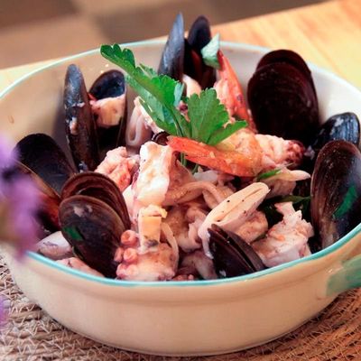 Un tazón blanco lleno de mariscos, incluidos mejillones y camarones.