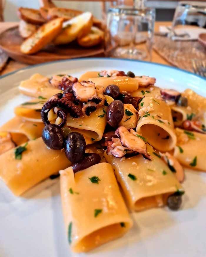 Un plato de pasta con pulpo y aceitunas sobre una mesa.