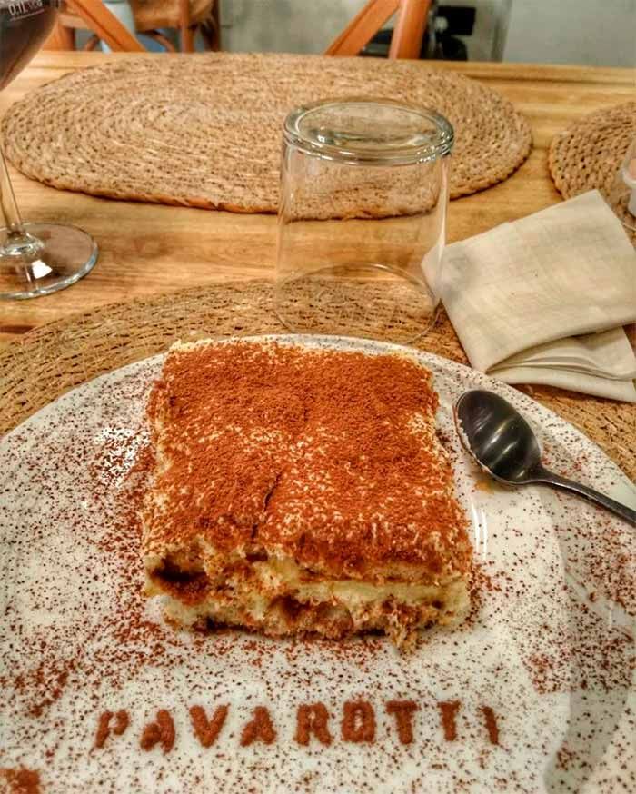 Un trozo de tiramisú en un plato con el nombre Pavarotti escrito en él.