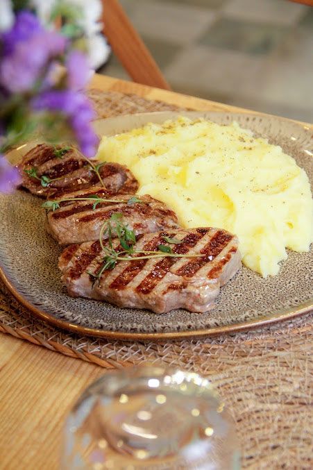 Un plato de comida con carne y puré de patatas en una mesa.