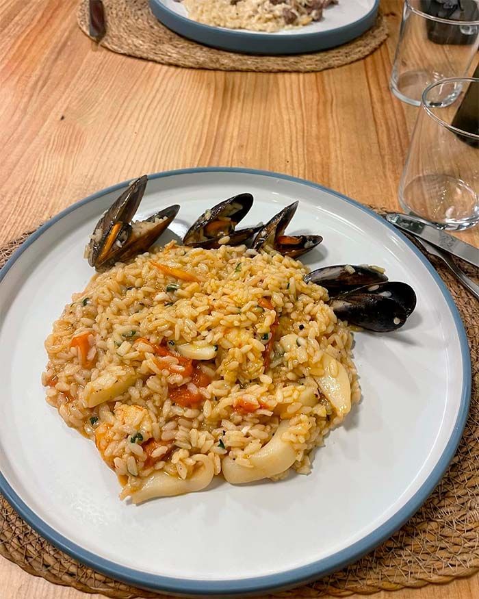 Un plato blanco cubierto con arroz y mariscos sobre una mesa de madera.