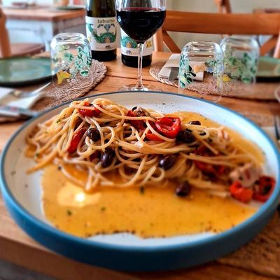 Un plato de espaguetis está en una mesa junto a una copa de vino.