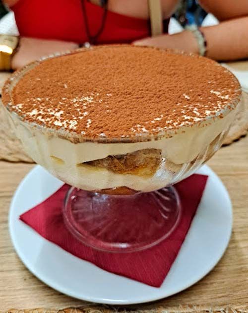 Un postre de tiramisú en un bol de cristal sobre un plato blanco.