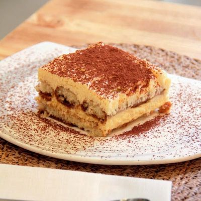 Un trozo de tiramisú está en un plato blanco sobre una mesa.