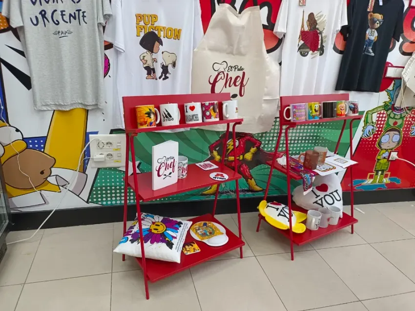 Exhibición de ropa con estantes rojos, camisetas estampadas coloridas y juguetes de peluche en una zona de tienda con azulejos.
