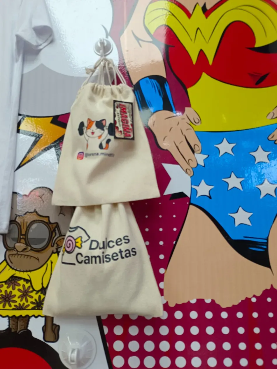 Dos bolsas de tela color crema colgadas en una colorida pared estilo cómic, una impresa con “Dulces Camisetas” y el logotipo del oso.