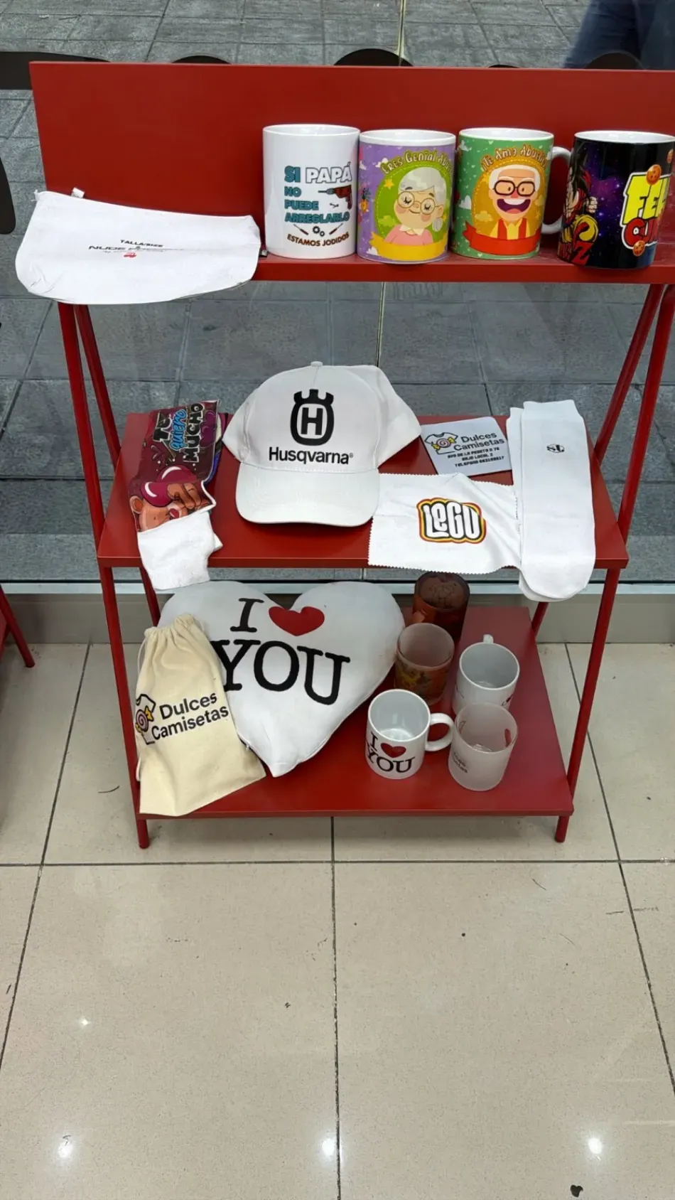 Estante rojo con tazas, gorras, camisetas, botellas y otros artículos personalizados impresos.