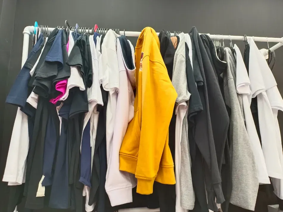 Ropa colgada en un perchero, incluyendo una sudadera amarilla brillante entre prendas grises, blancas y negras.