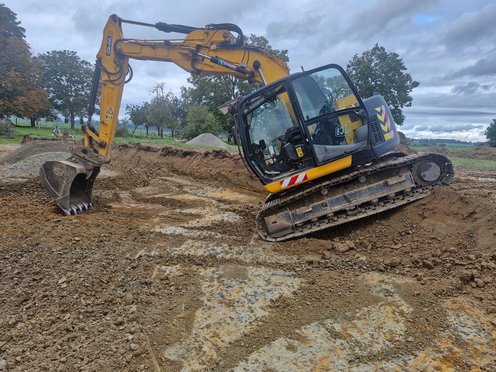 Une pelleteuse jaune inclinée sur un terrain boueux sur un chantier de construction sous un ciel nuageux.